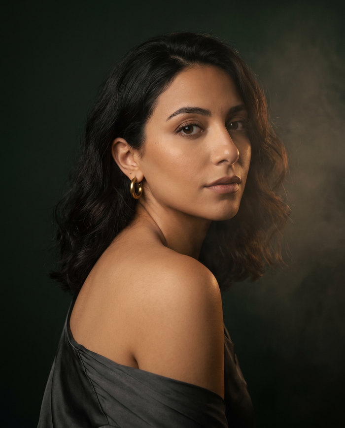 A woman glances over her shoulder from deep evening shadow, gold light on her cheek.