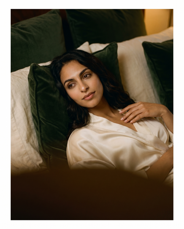An elegant woman reclines in warm amber light against ivory linen and forest-green velvet, a moment of indulgent ease.